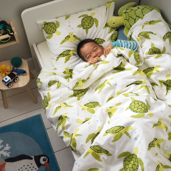 Child sleeps on turtle-patterned bedding with toys and blanket.