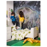 Kids drawing on large chalkboard wall beside a bed covered with a green and white turtle-patterned duvet.
