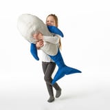 A girl hugging a large blue whale plush toy. The toy is designed for comfort, play, and has safety-tested.