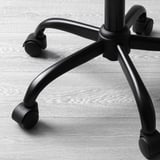Close-up of black office chair base. Five castors, robust metal arms, and sturdy star-shaped frame. Resting on wooden floor.