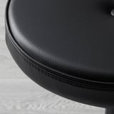 Close-up of smooth, round, black leather chair seat, showcasing high-quality stitching and texture.