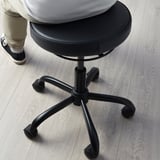 Person sitting on BLYKOBB active stool with leather seat, five-star base, and wheels.