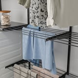 Black drying rack with clothes: jeans, shirt, towels.