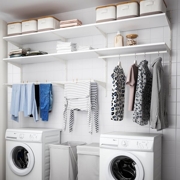 Modern laundry setup: white BOAXEL wall system holds clothes, bins, and dryer. Clothes hang neatly below, with washer/dryer pair beneath.