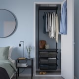 Modern blue bedroom with grey BOAXEL closet, neat clothes, and nightstand lamp.
