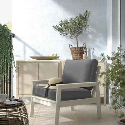 Modern outdoor lounge area with BONDHOLMEN gray cushioned chair, white cabinet, and green plant.