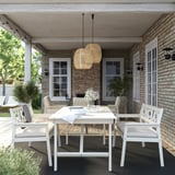Modern outdoor dining set with white bondholm white chairs, rectangular table, and natural pendant lights on brick patio.