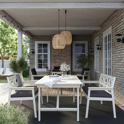 White dining set with dark cushioned chairs, glass vase of flowers, rug, and pendant lamps under porch, welcoming ambiance.