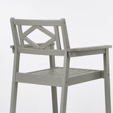 Displays a high-quality, grey outdoor chair made of durable eucalyptus. It a traditional style with handicraft details and plastic feet for stability.