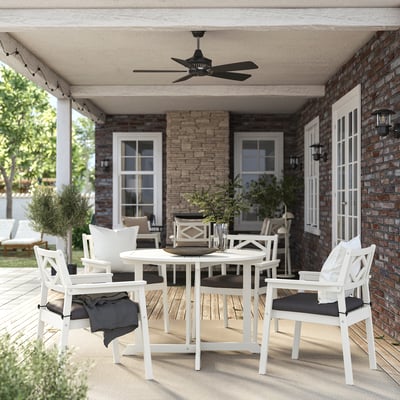 Cozy patio with white BONDHOLMEN outdoor furniture set under a black ceiling fan on brick house, including a round dining table and cushioned chairs.