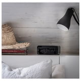 Black BONDTOLVAN alarm clock on nightstand with lamp, hat, wooden wall.