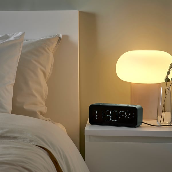 Bedside scene with BONDTOLVAN alarm clock displaying time, 11:30 pm, on a nightstand beside a modern lamp and beige pillows.