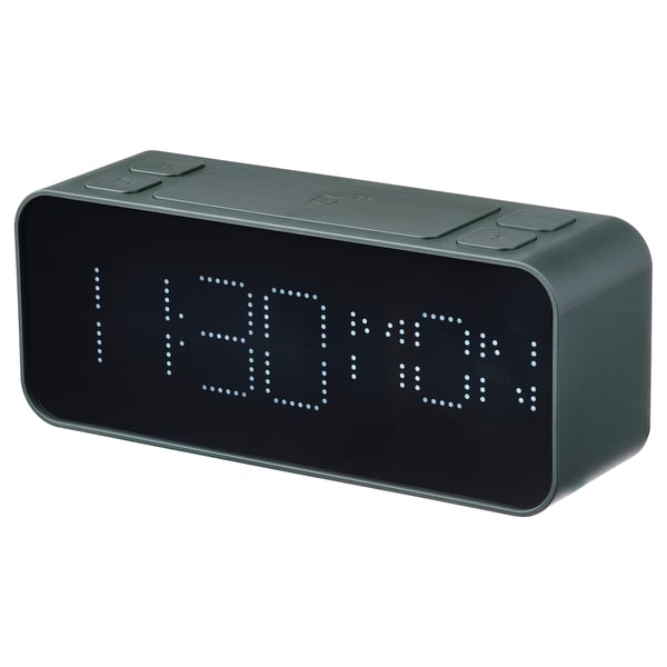 A digital alarm clock in dark green, displaying time and day, made from recycled plastic, designed by aaron probyn.