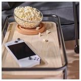 Wooden side table with castors holds popcorn bowl and handheld device, ideal for gaming and snacks.