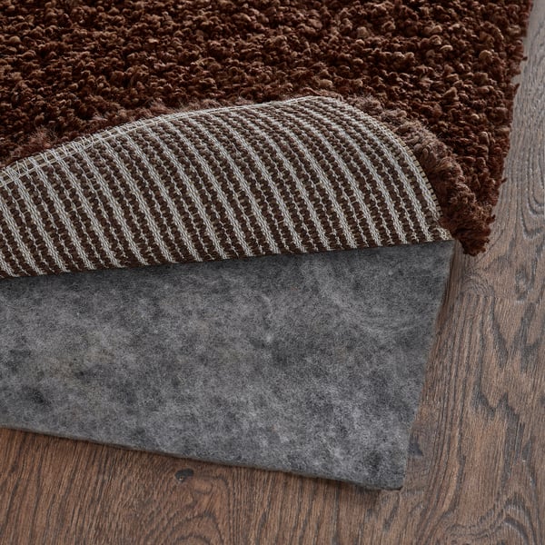 A close-up of a rugs edge, showing its thick pile and grey non-slip mat underneath.