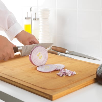 A person is slicing an onion on a wooden cutting board using a large, sharp knife. Finely chopped onion pieces are already on the board.