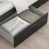Bed with open storage drawers: one with folded linens, another with blanket, ideal for small spaces.