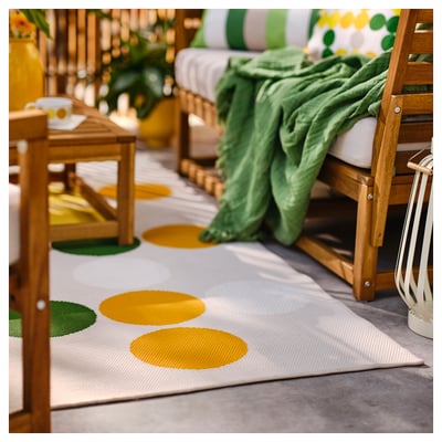 Yellow-green rug with circles on balcony furniture, blanket, plants