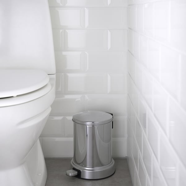 Silver trash pedal bin in bathroom beside white toilet with closing lid.
