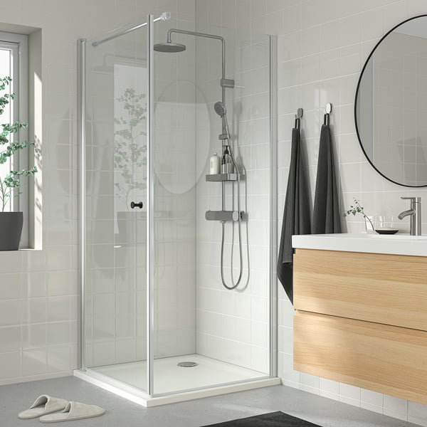 Modern bathroom with BROGRUND shower, glass door, chrome, minimalist design. White tiles, dark towels, wooden vanity.