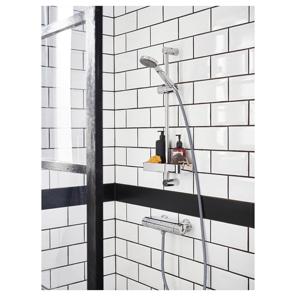 Modern chrome shower setup with adjustable shelf for soap dispensers and spa products, on white tiled wall with black stripe.