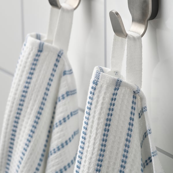 Two white towels with blue accents hang on metal hooks. One shows textured waffle side, the other soft terry side.