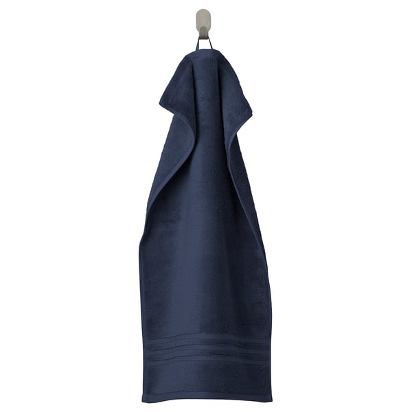 A dark blue BROKGLIM towel hangs neatly on a hook. Made of soft, absorbent organic cotton with a woven border.