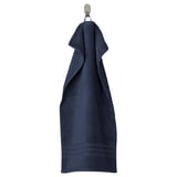 A dark blue BROKGLIM towel hangs neatly on a hook. Made of soft, absorbent organic cotton with a woven border.