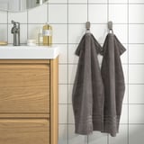 Gray towels on hooks by modern vanity with gold toiletries.