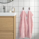 Bathroom scene with light pink BROKGLIM towels hanging, matching white sink, wooden cabinet, and modern decor. Sleek and organized look.