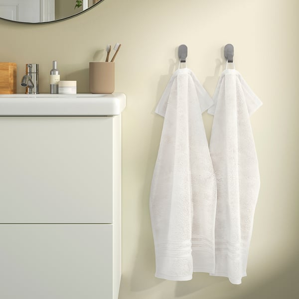Two white towels hang on hooks beside a white vanity with toiletries. A mirror reflects part of the room.