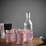 Four pink BROKROCKA glasses and a bottle on a wooden table.