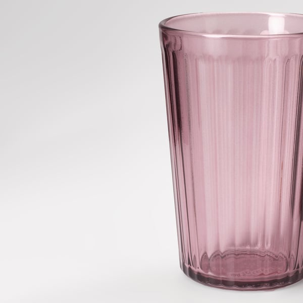 Single, tall, clear glass with vertical ridges, colored in soft pinkish hue, placed on white background.