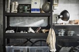 Black metal storage unit with various tools and containers on shelves. Includes a wall-mounted black lamp.