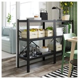 Black metal storage shelf named BROR, versatile for kitchen or dining room, holding wooden crates with fruits and kitchenware.