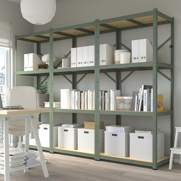 A BROR green metal storage rack with multiple shelves holding books and boxes. Its large compared to the desk and chair.