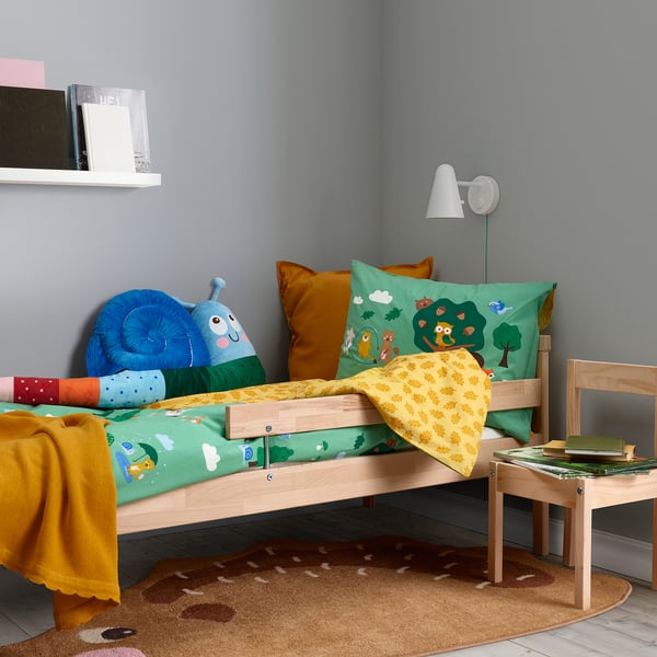 Kids bedroom with green/yellow BRUMMIG bedding, small bed, plush blue snail, books, wall lamp, deer rug.
