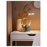 Modern desk with green BRUNBÅGE lamp, white vase, dried flowers, headphones, pens, and notebooks.