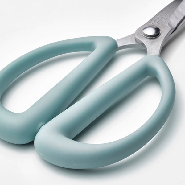 A pair of small, sharp scissors with comfortable green handles lies open on a white surface, ideal for precise trimming of plants or herbs.