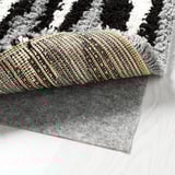 Black and white shaggy area rug partially rolled up, revealing its plush quality and a gray rug pad underneath.