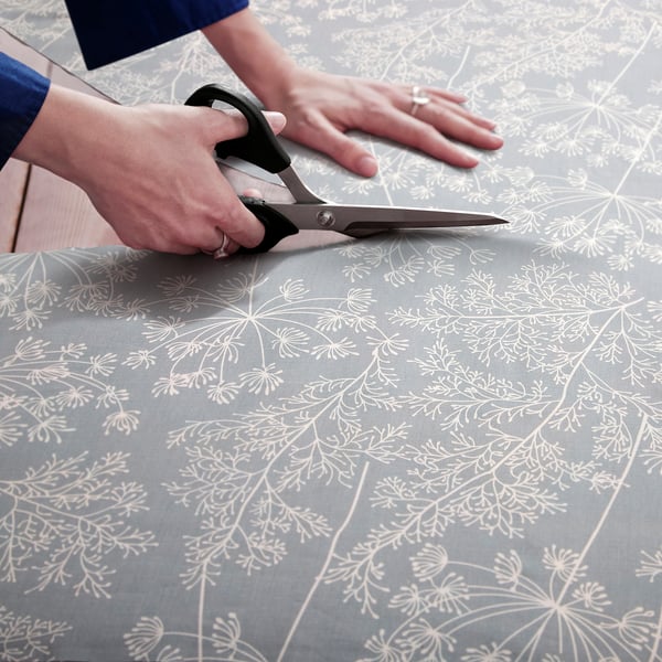 Person cutting grey fabric with white floral pattern. Item used for diy sewing projects like curtains or crafts.