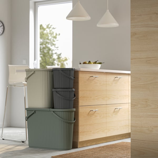 Three stacked DAMMÄNG bins near wooden cabinets, perfect for small waste like light bulbs. One bin has a lid, indicating waste storage function.