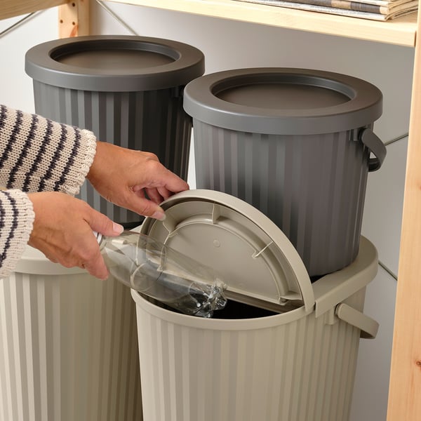 Person discards glass bottle into gray stackable DAMMÄNG recycling bin, highlighting its use for recycling and space-saving design.