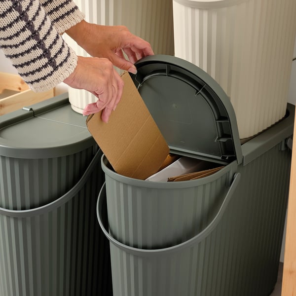 Person disposing of cardboard box into DAMMÄNG recycling bin with lid open.