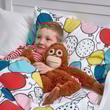 A child hugs a soft toy monkey, which can be used to hang on a backpack, demonstrating its functional design.