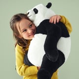 A child in a yellow sweater hugging a large plush panda toy.