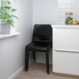 A sleek black DOCKSTA chair tucked neatly next to kitchen cabinets, showcasing its space-saving design and modern appeal.