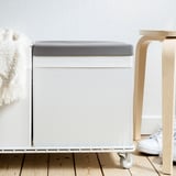 Grey fabric box lid on wooden floor with chair and coat hanger.