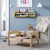 DUKTIG wooden kids bed, blue, with bear & blanket. Near shelf with books, small bedside table, and larger white bed. Cozy, small, & colorful.