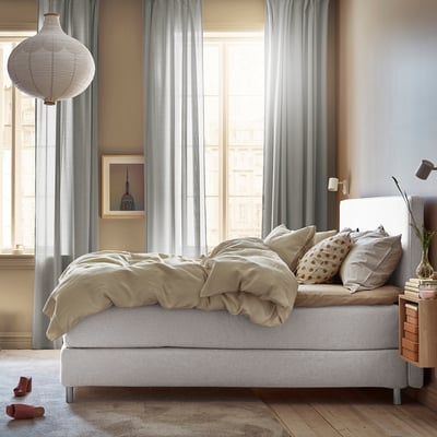 Minimalist bedroom: white DUNVIK bed, beige linens, large window, grey curtains, and wall art.